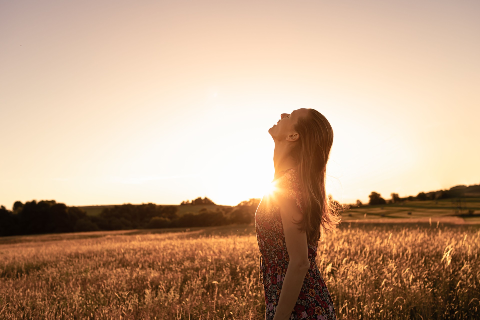 Joyful young beautiful woman standing in a field at sunset looking up to the sky feeling happy.
